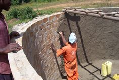 two men standing next to each other near a brick wall and cement blocks in front of them