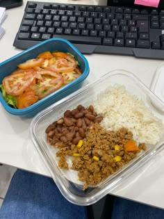 a plastic container filled with rice, beans and meat next to a keyboard on a desk