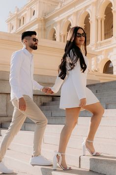 a man and woman holding hands while standing on some steps in front of a building