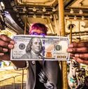 two people holding up one dollar bill in front of another person's face and hands