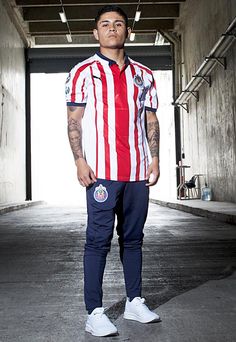 a man standing in an empty room with his hands on his hips wearing a red, white and blue striped shirt