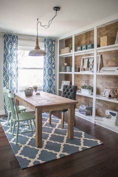 a dining room table and chairs in front of a bookshelf with blue curtains