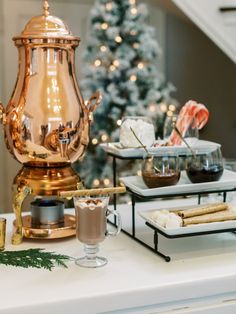 A cup of hot cocoa on a white table surrounded by holiday-themed decor and assorted toppings. Christmas Wedding Hot Chocolate Bar, Hot Drink Bar Wedding, Elegant Hot Cocoa Bar, Wedding Hot Cocoa Bar, Hot Chocolate Bar For Christmas, Hot Chocolate Station Ideas, Hot Cocoa Bar Wedding, Christmas Hot Chocolate Station, Wedding Hot Chocolate Bar