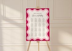 a pink and white wedding seating chart on a easel in front of a wall