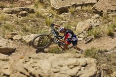 a man riding a mountain bike down a rocky trail in the desert with grass and rocks