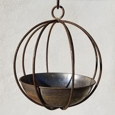 a metal bowl hanging from a hook on a white wall with an iron ring around it