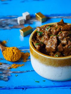 a small bowl filled with meat and spices next to some cubes of food on a blue surface