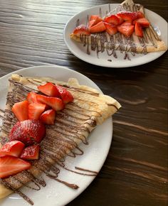 two white plates topped with pancakes covered in syrup and strawberries