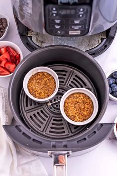 three bowls filled with granola sitting on top of a counter next to fruit and an air fryer