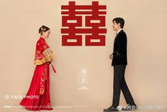 a man and woman standing next to each other in front of a wall with chinese characters on it