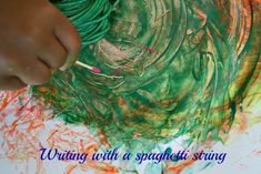 a child's hands painting with green and orange paint