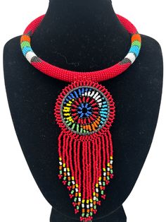 Add a touch of African beauty to your outfit with this beaded necklace. Handcrafted using high-quality beads and brass metal, this necklace is a perfect addition to any jewellery collection. The pendant's unique tassel design adds a touch of elegance to its ethnic and regional style. Its red colour symbolizes passion and love, making it a great gift to show appreciation to a loved one. This necklace is perfect for any occasion, from a casual day out to a formal event. With its intricate beaded design, it is sure to catch the eye of anyone who sees it. Whether you wear it to work or a night out, this necklace will add a touch of glamour to your outfit.  Neck Width - 18 inches. Colour: Red Material: Beads, Brass Red Tassel Necklaces For Gifts, Red Tassel Necklaces As Gifts, Red Tassel Necklace For Gift, Traditional Beaded Fringe Necklace, Traditional Beaded Fringe Necklace As Gift, Traditional Red Jewelry With Tassels, Red Round Beads Jewelry With Tassels, Red Tassel Jewelry With Round Beads, Artisan Red Beaded Necklace With Dangling Beads