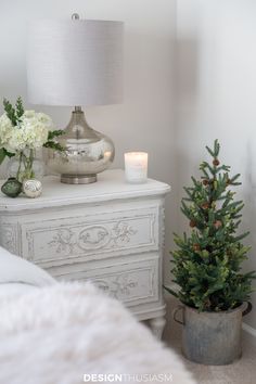 a small christmas tree sitting on top of a white dresser next to a lit candle