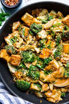 broccoli and tofu stir fry in a skillet with sauce on the side