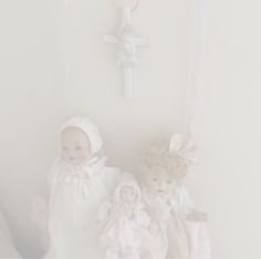 two dolls are sitting in front of a wall with a cross hanging from it's side