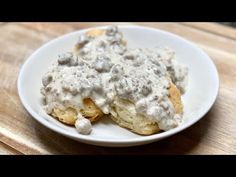 a white plate topped with biscuits covered in gravy on top of a wooden table