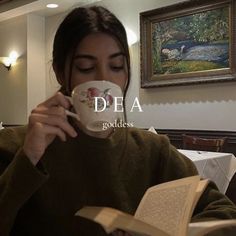 a woman is drinking from a cup and reading a book with the words dea on it