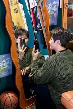 two boys sitting in front of a mirror looking at their cell phones and taking pictures