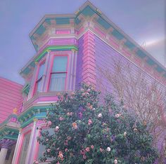 a pink and blue house with roses on the tree in front of it's windows