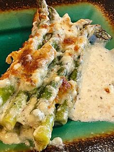 a green plate topped with asparagus covered in gravy next to a white sauce