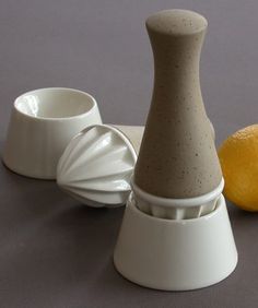 a small white vase sitting on top of a table next to a lemon and two cups