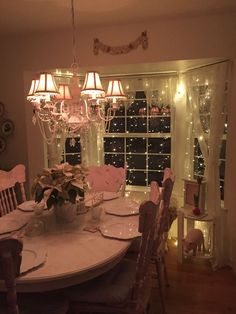 the dining room table is set for dinner with pink chairs and chandelier in the background