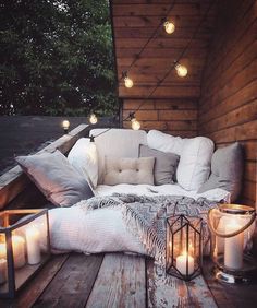 a couch sitting on top of a wooden deck covered in pillows and lights next to a lantern