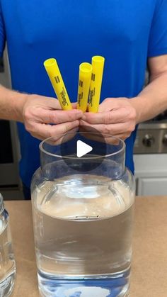 the man is holding yellow markers in his hand near a glass of water and ice cubes