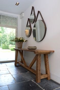 a wooden table sitting next to a wall with mirrors on it's sides and two vases filled with flowers