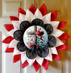 a red and white wreath hanging from the front door with a cross on it's center