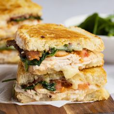 two sandwiches stacked on top of each other next to a bowl of greens and sauce