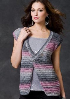 a woman wearing a gray and pink knitted cardigan over her shoulder, standing in front of a dark background