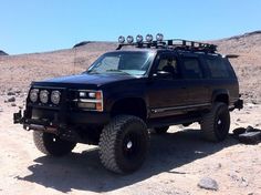 a black suv parked in the desert with its lights on and four wheel drive tires