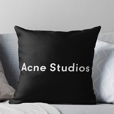 a black pillow with the words acne studios in white on it sitting on a couch