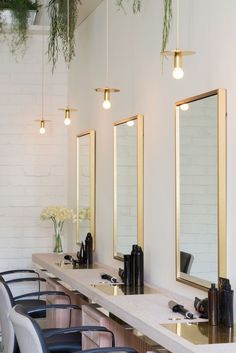 a row of sinks sitting under three mirrors in a room with plants hanging from the ceiling