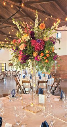 a tall vase filled with lots of colorful flowers on top of a table covered in wine glasses