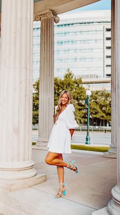 a beautiful woman posing in front of some white pillars with her legs crossed and wearing high heels