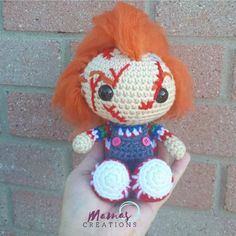 a small crocheted doll with orange hair sitting in front of a brick wall