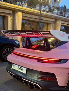 a pink sports car parked in front of a building with its surfboard on it's roof