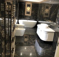 a bathroom with black marble walls and flooring, two white bathtubs next to each other