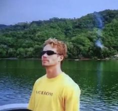 a young man standing on top of a boat in front of a lake with trees