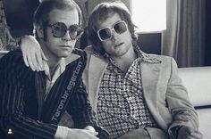 two men sitting next to each other in front of a window wearing sunglasses and jackets