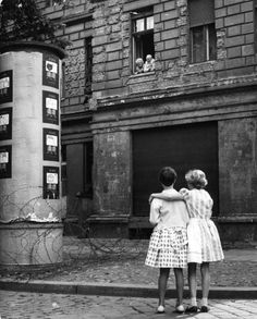 two girls hugging each other in front of a building with an inscription on the back