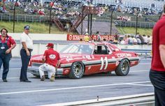 a man sitting on the back of a red race car in front of a crowd