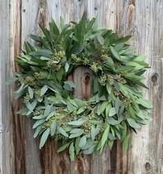 a wreath is hanging on the side of a wooden fence with green leaves and flowers