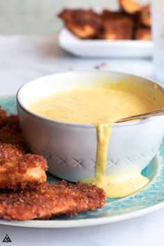 a white bowl filled with cheese sauce next to some fried chicken strips on a plate