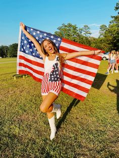 a woman holding an american flag in the grass with her arms outstretched and legs crossed