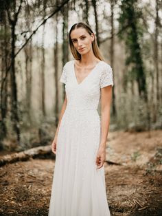 a woman standing in the woods wearing a white dress