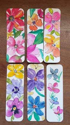 four flower bookmarks are sitting on a wooden table with watercolor flowers painted on them