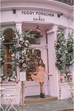 a woman standing in front of a flower shop with pink flowers on the windows and doors